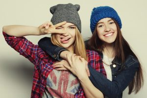 Two young girl friends standing together and wearing beanies.