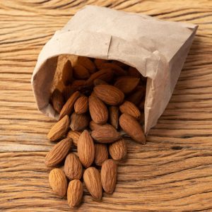 Almonds in a paper bag over wooden table.